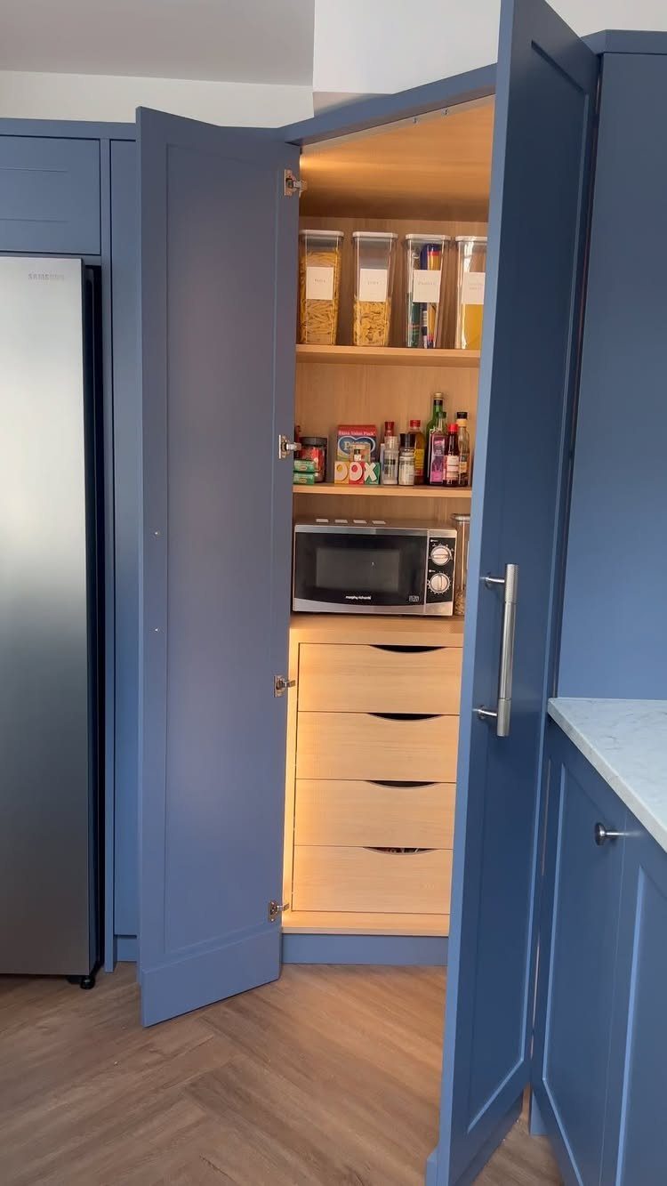 Open blue pantry cabinet showing organized wooden shelves with food containers and a microwave.