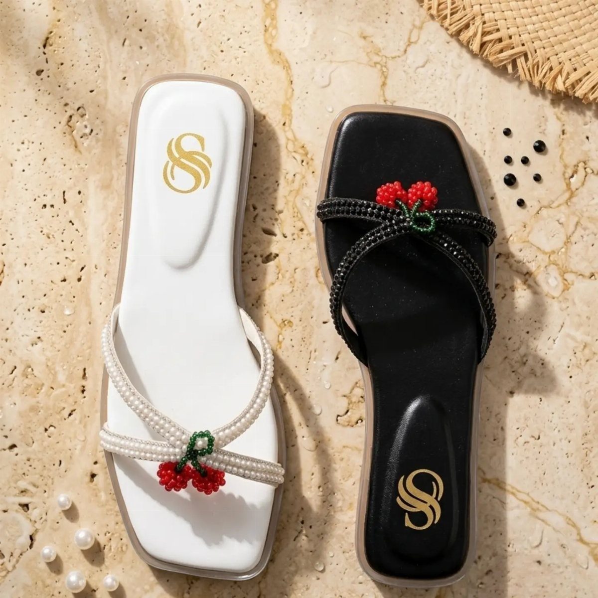 White and black beaded sandals with small red cherry decorations on a beige surface.