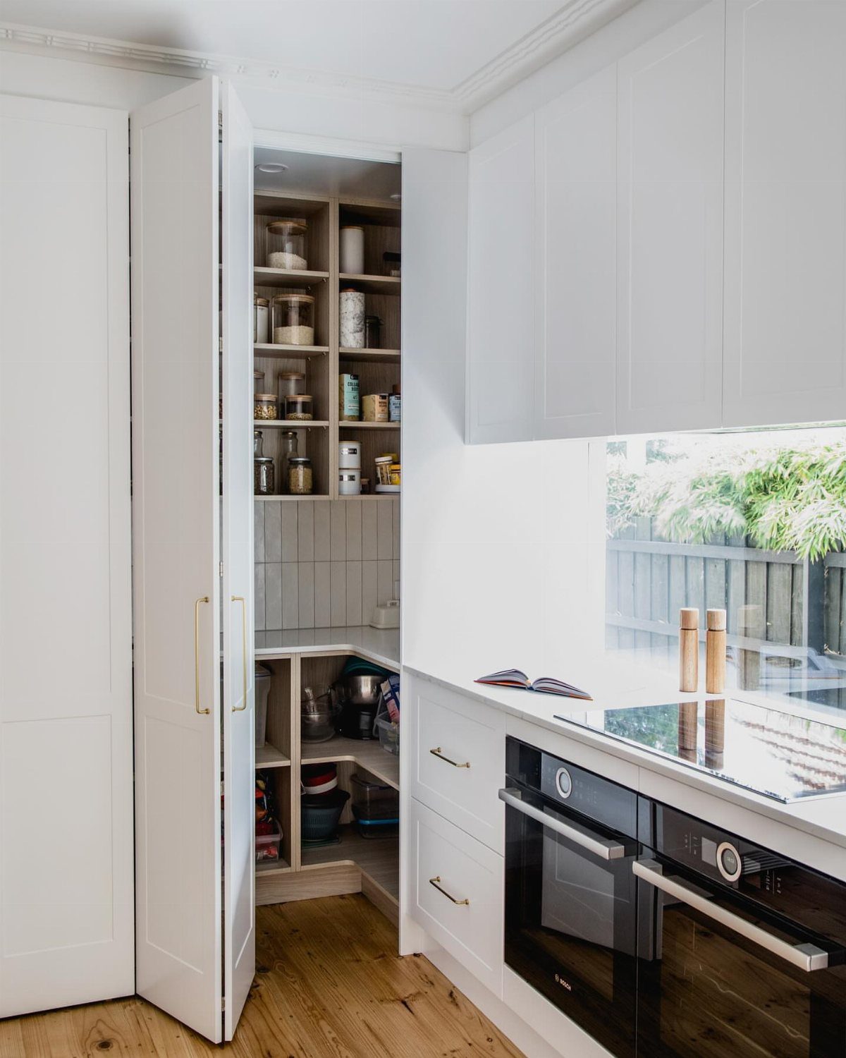 White kitchen cabinets and an open pantry with warm wooden shelving and light wood floors.