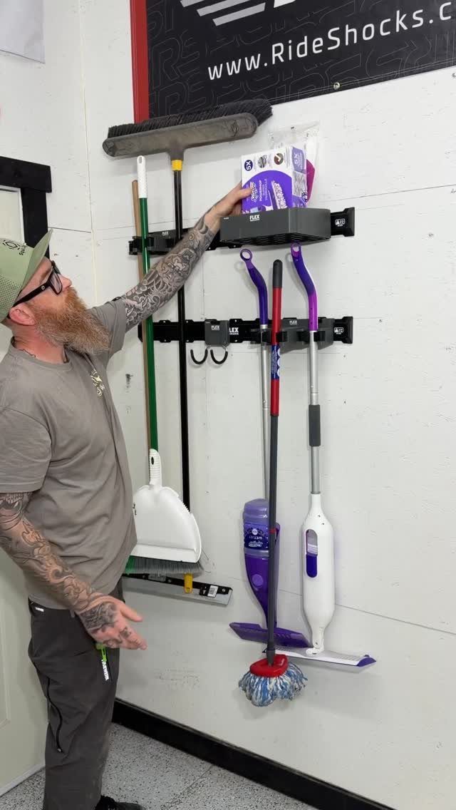 A man reaches for a box on a wall-mounted rack holding mops and brooms.