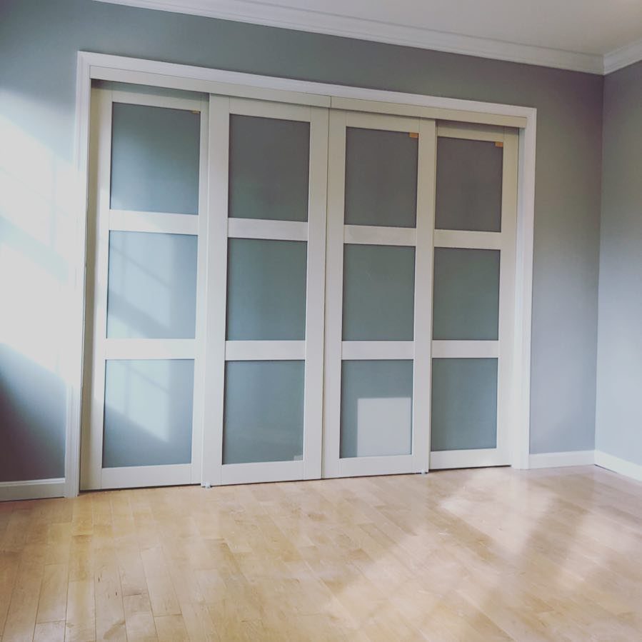 Four white sliding closet doors with frosted glass panels in a light blue room.