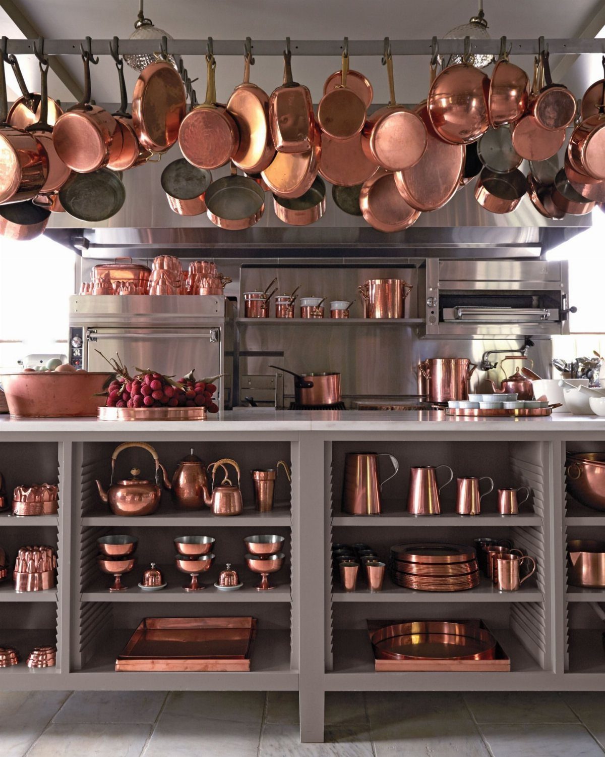 Numerous copper pots and pans hanging from a rack and displayed on kitchen shelves.