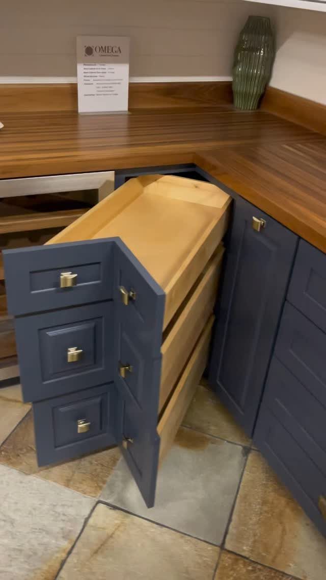 L-shaped corner drawers pulled out from blue kitchen cabinetry under a wooden countertop.