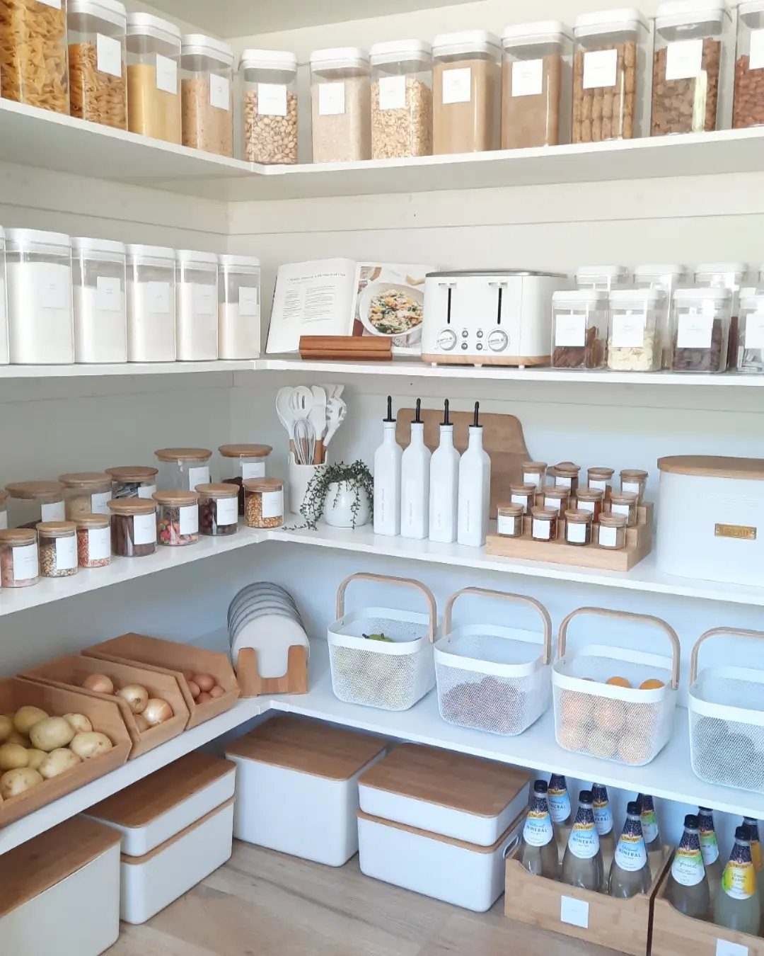 Organized pantry shelves featuring various labeled clear containers, glass jars, and wooden storage bins.
