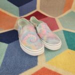 Pastel tie-dye canvas slip-on shoes resting on a colorful geometric rug.