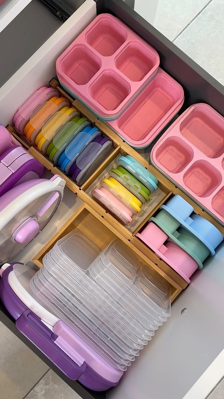 Various colorful bento lunch boxes and clear containers organized inside a wooden drawer divider.
