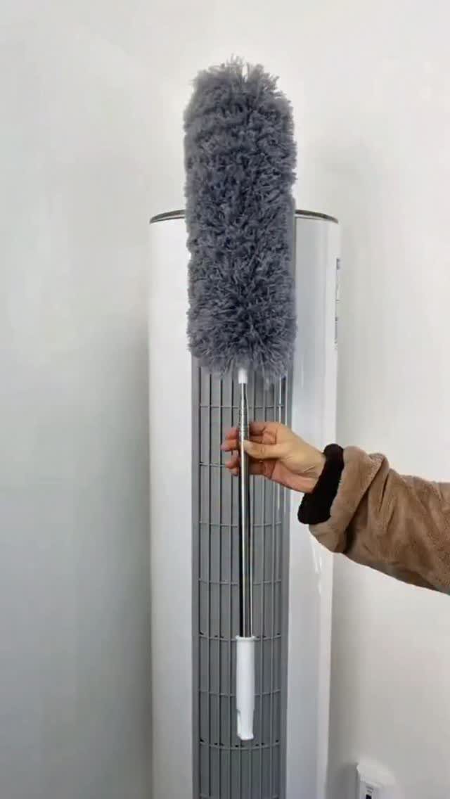 A hand holding a long grey fluffy extendable duster against a white appliance.