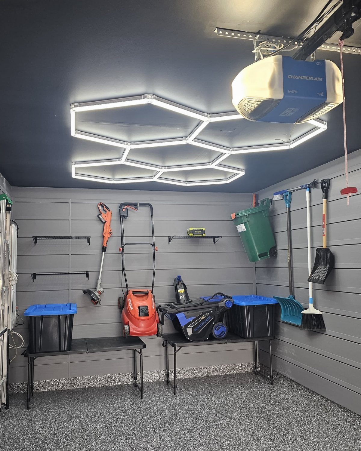 Organized garage with slatwall, folding tables, lawnmower, and hexagonal LED ceiling lights.