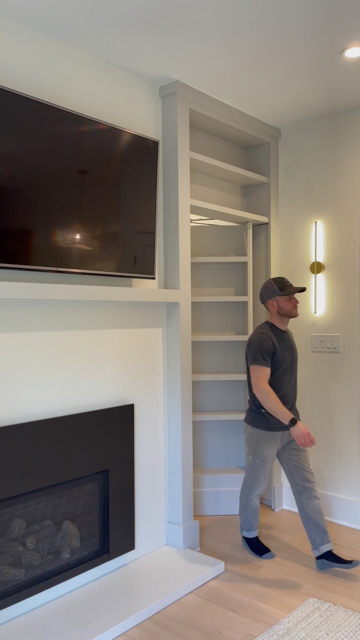 A tall white built-in bookshelf standing next to a modern fireplace and television.