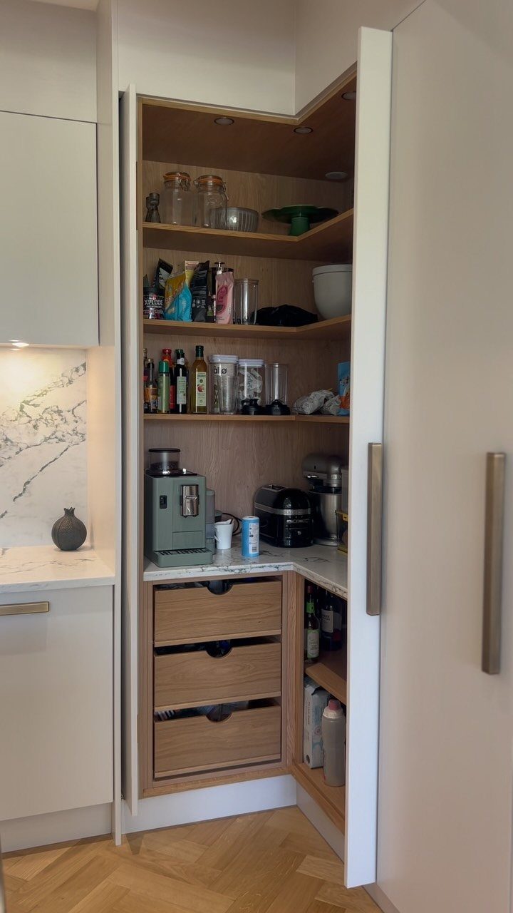 An open corner pantry with wooden shelves and drawers filled with various kitchen supplies and appliances.