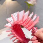 Hands bending a flexible pink and white scrubbing brush against a white background.