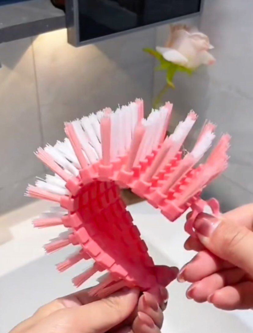 Hands bending a flexible pink and white scrubbing brush against a white background.