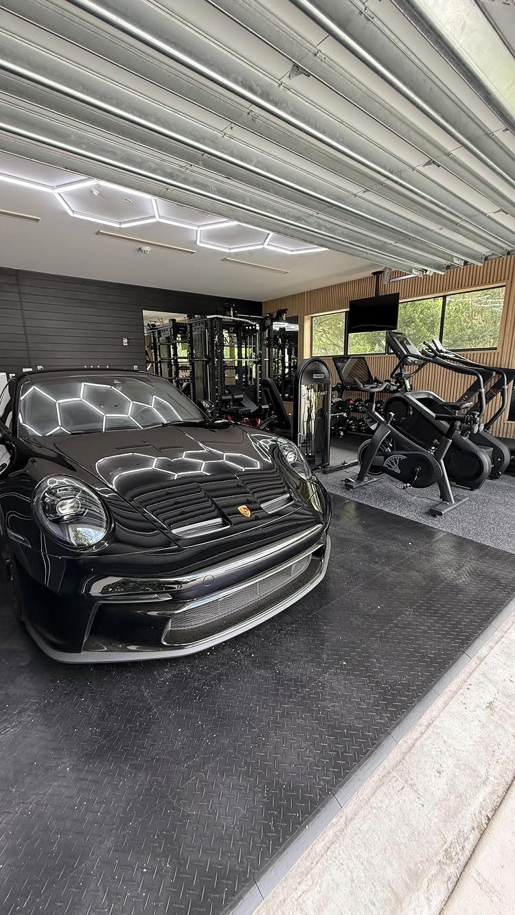 Black luxury car parked in a modern garage with gym equipment in the background.