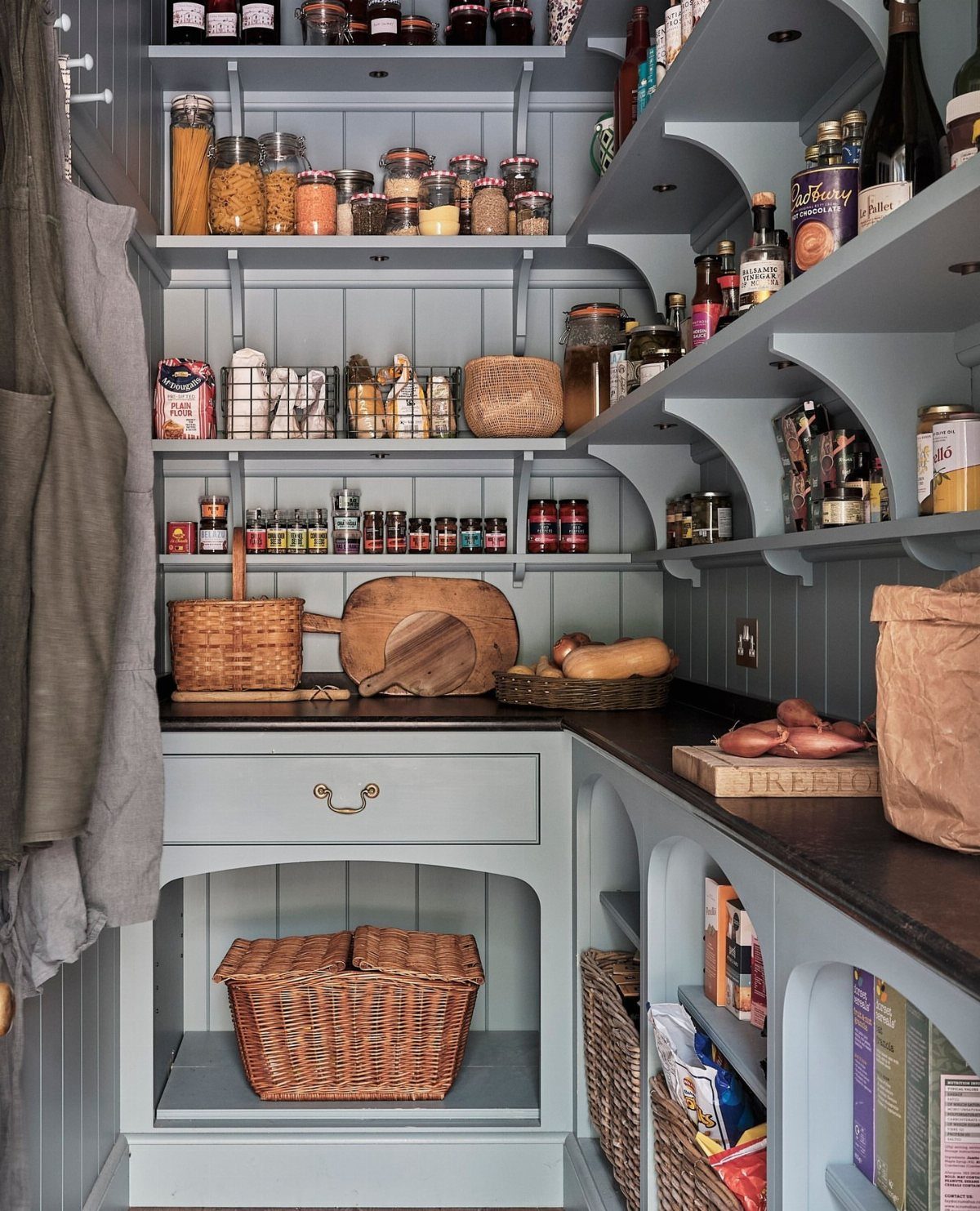 Light blue pantry shelves filled with glass jars, spices, and wicker baskets on a dark countertop.