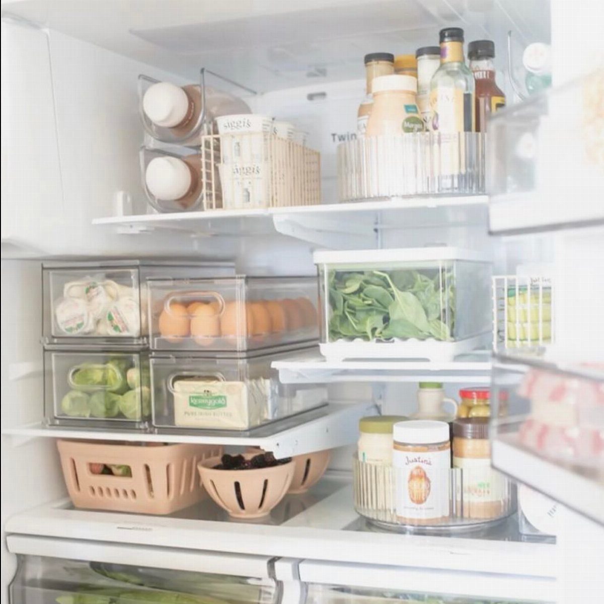 Organized refrigerator shelves containing clear storage bins, eggs, greens, and a rotating condiment turntable.