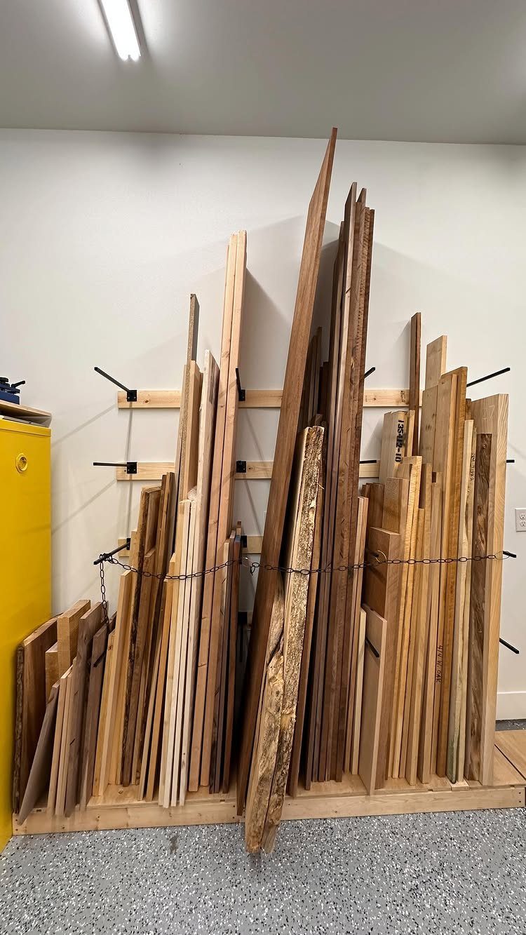 Vertical wooden planks stored in a custom-built wooden rack against a white garage wall.