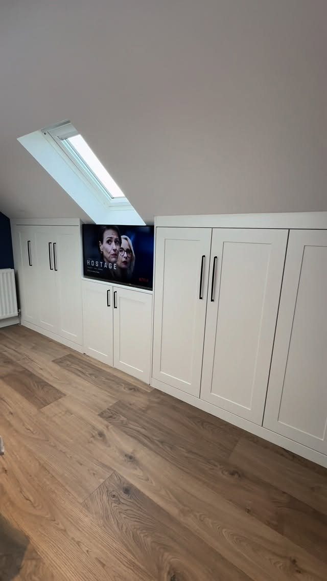 White built-in storage cabinets installed under a sloped attic ceiling with a skylight.