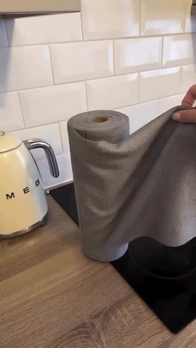 A hand pulls a grey microfiber cloth from a large roll on a kitchen counter.