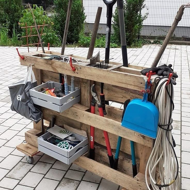 A wooden pallet storage cart holding various garden tools and grey plastic bins on a patio.