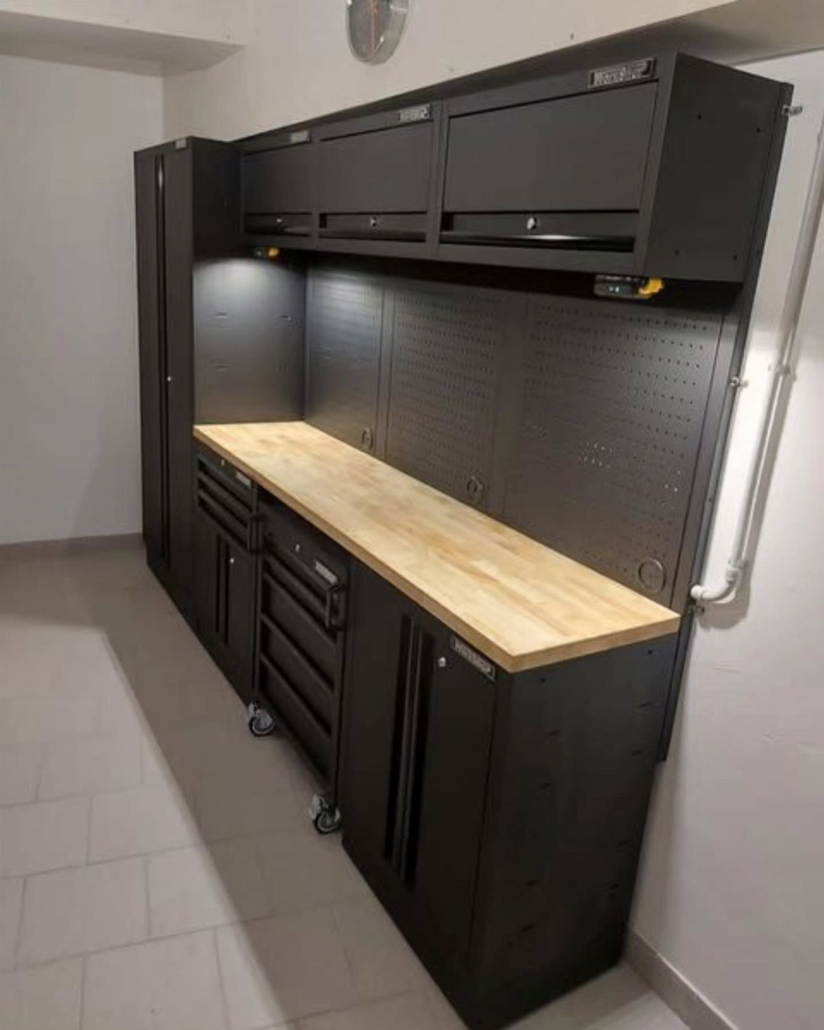 Black garage workstation with a light wood countertop and integrated tool storage cabinets.