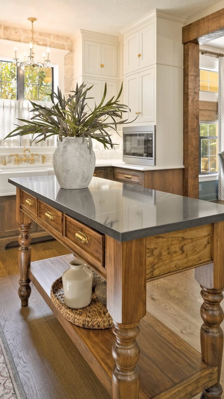 A wooden kitchen island with a dark stone countertop and turned legs in a bright kitchen.