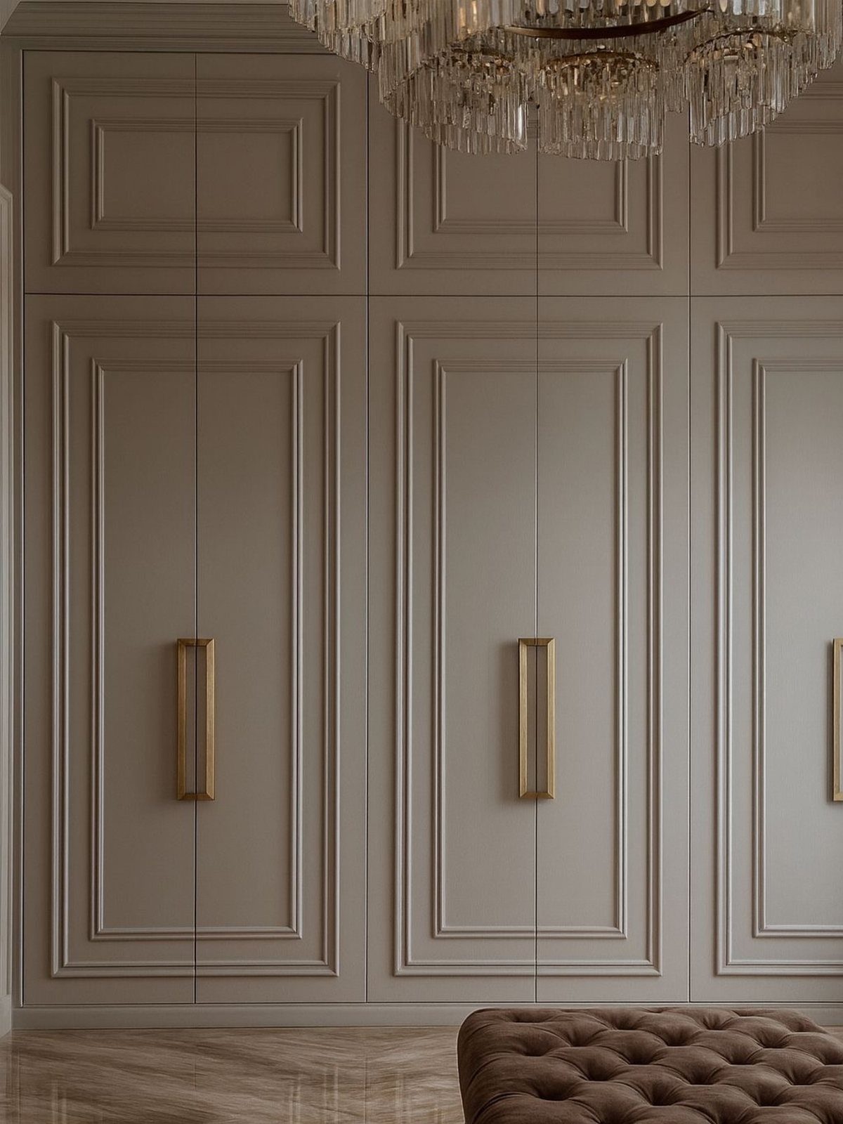 Taupe paneled closet doors with long gold handles and decorative molding in a luxury room.