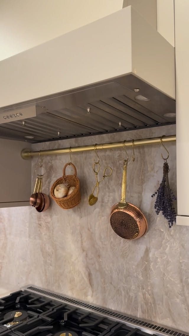 Brass pot rail hanging copper cookware and kitchen utensils against a marble backsplash.