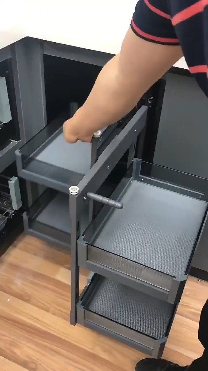 A hand pulling out a grey metal pull-out shelf from a dark kitchen cabinet.