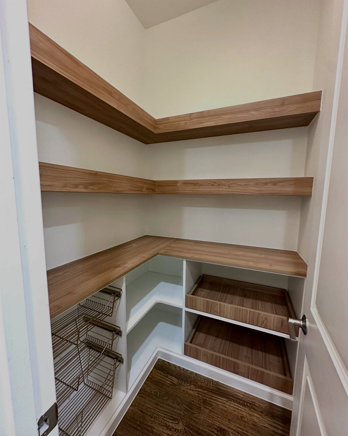 Empty corner pantry featuring wooden shelves and pull-out wire and wood storage drawers.