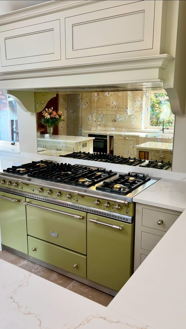 An olive green range cooker with silver handles sits under a white mantelpiece.
