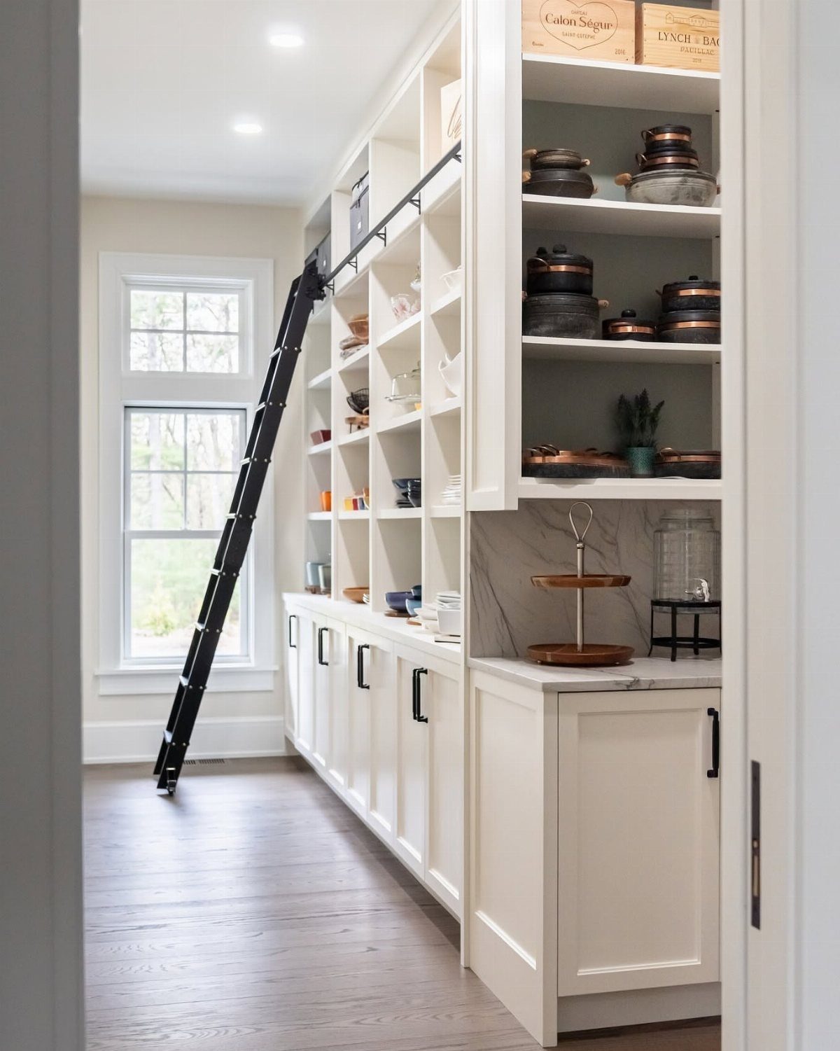 White built-in pantry cabinets with open shelving and a black rolling library ladder.