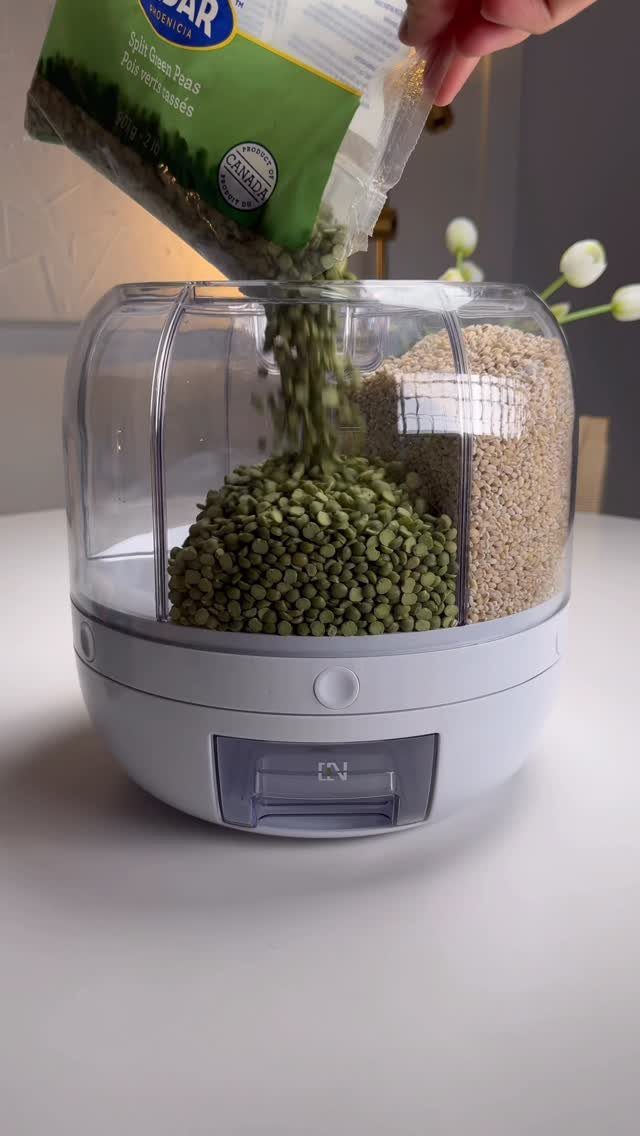 Green split peas being poured from a bag into a clear rotating food storage dispenser.