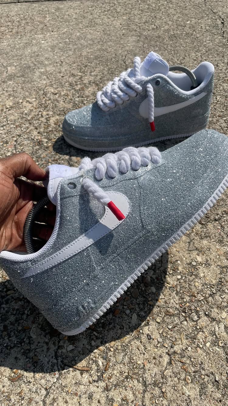 Silver glitter-covered Nike sneakers with white laces held against a concrete background.