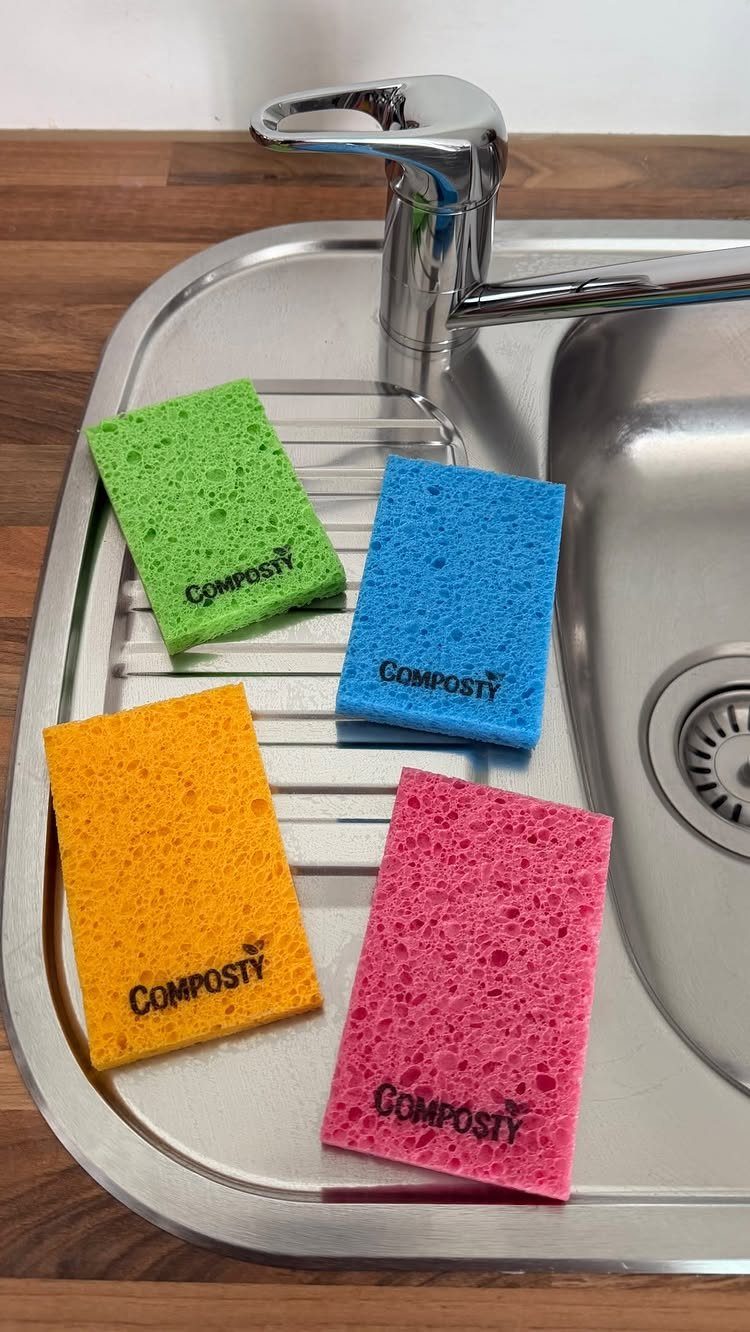Four colorful rectangular sponges in green, blue, yellow, and pink on a metal sink drainer.