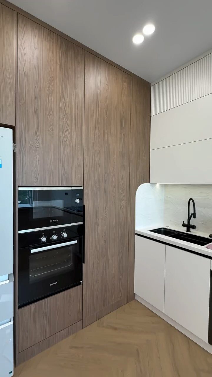 Tall wood-grain kitchen cabinets with a built-in black oven next to white cabinetry.