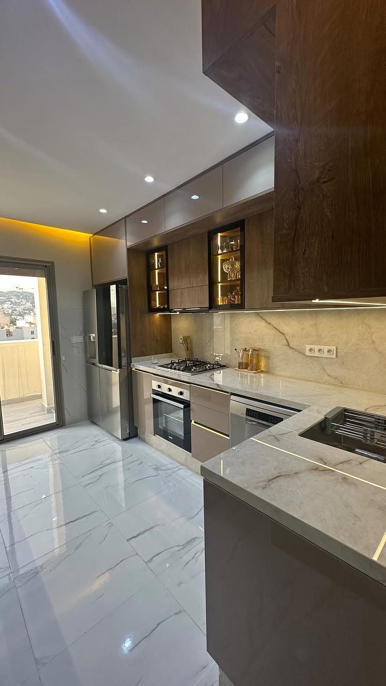 Modern kitchen with marble countertops, dark wood cabinets, and warm under-cabinet LED lighting.