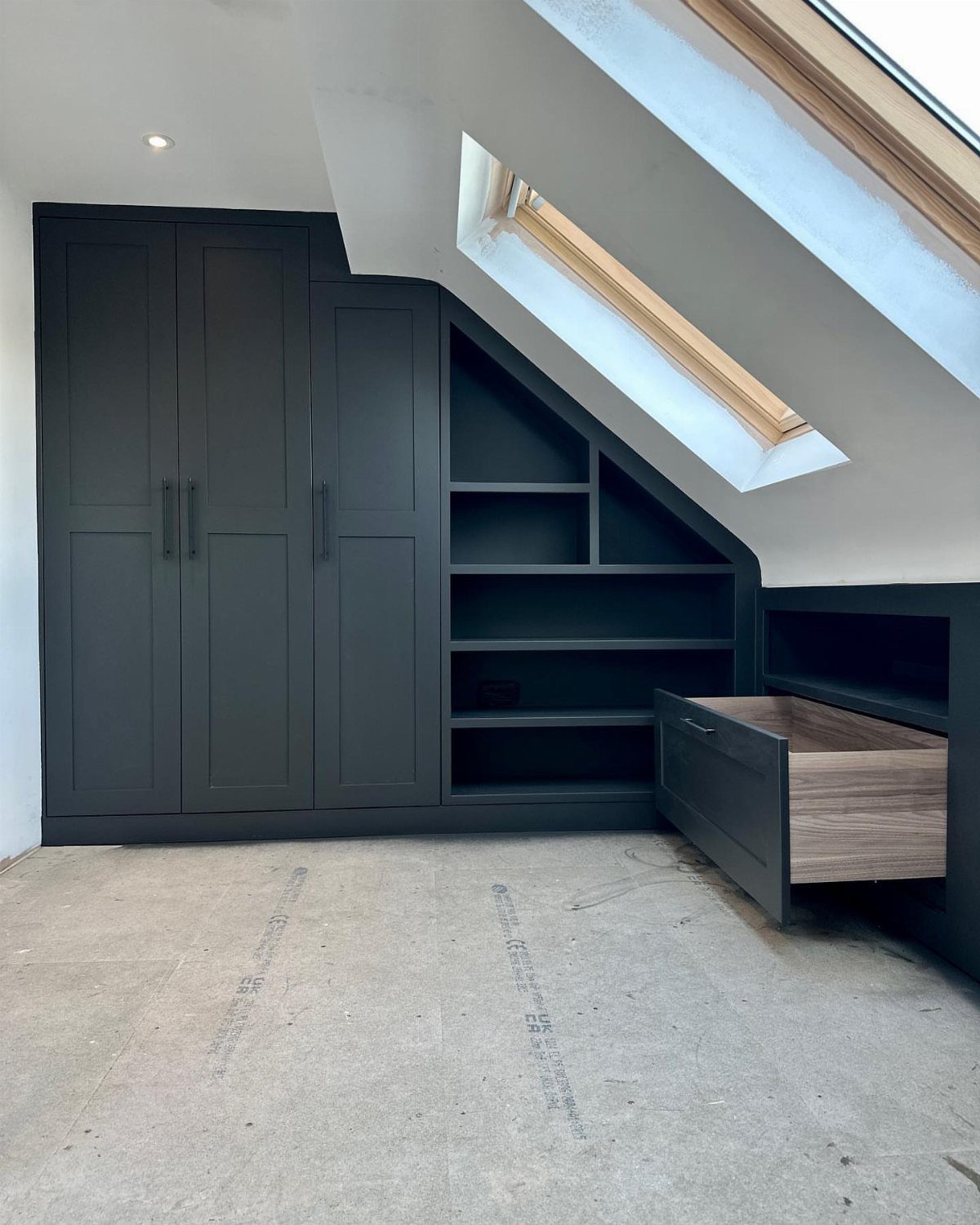 Dark grey built-in wardrobes and open shelving units installed under a sloped attic ceiling.