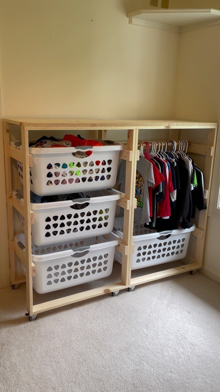 A wooden rolling frame holding white plastic baskets and hanging clothes in a room.
