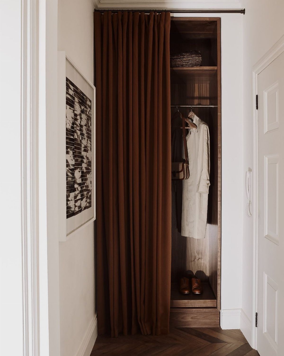 Brown fabric curtains covering an open wooden closet containing clothes and shoes.