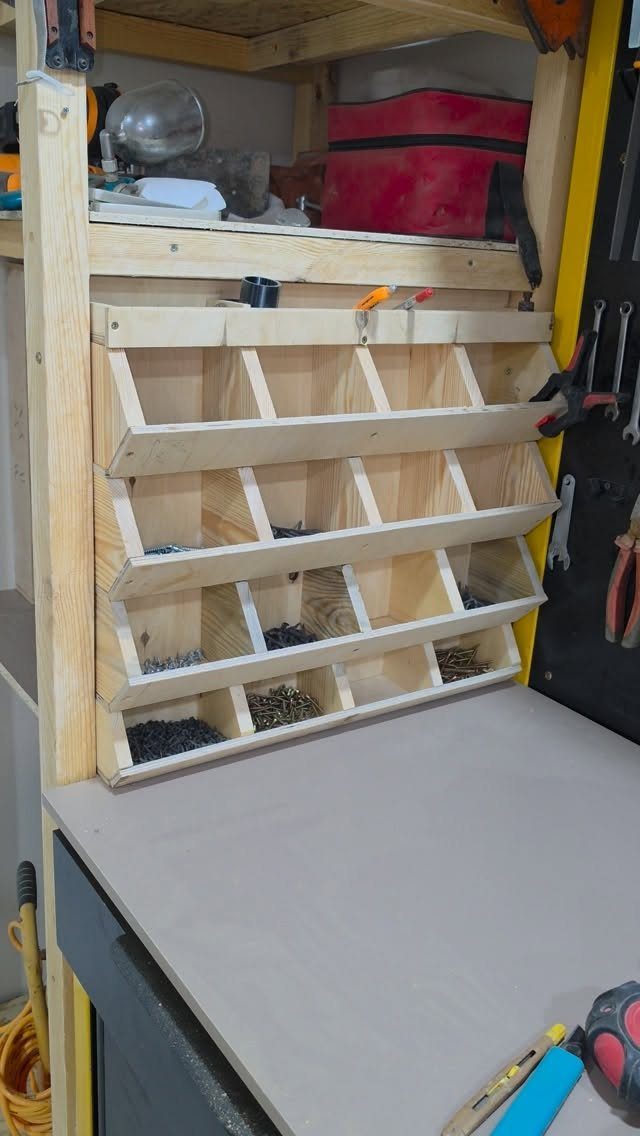 Wooden organizer with small open compartments filled with various metal screws and fasteners on a workbench.